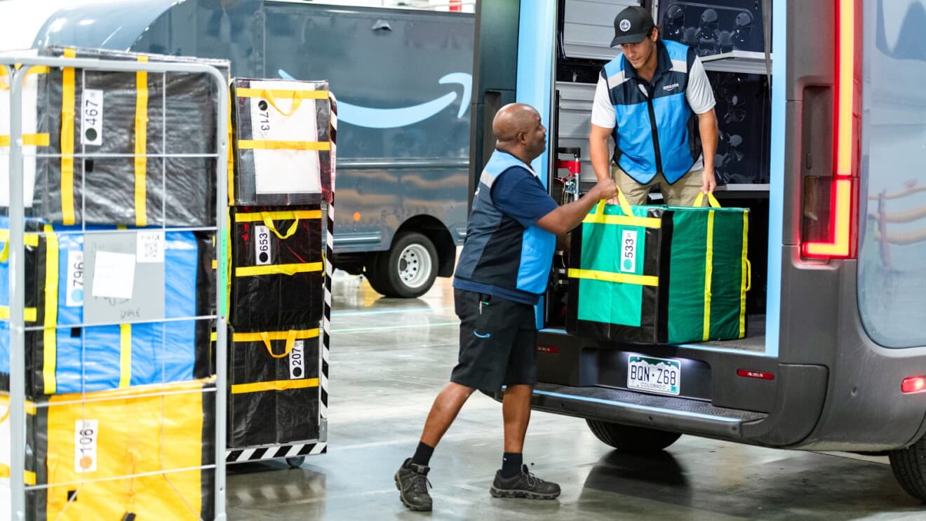 Two delivery associates loading package bags into an Amazon delivery van at the station